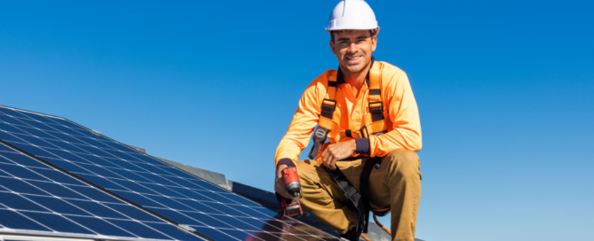 Installer kneeling near solar panels on top of roof while smiling