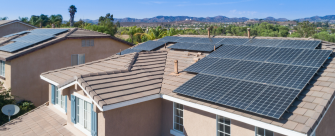 Photo shows solar panels on a large home with angled roof next to another home with solar panels installed