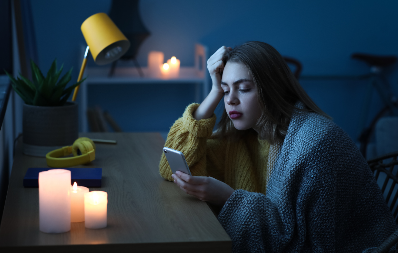 During a power outage, your solar battery can still bring you power. A girl is on her cell phone during a blackout using candles instead of light. 