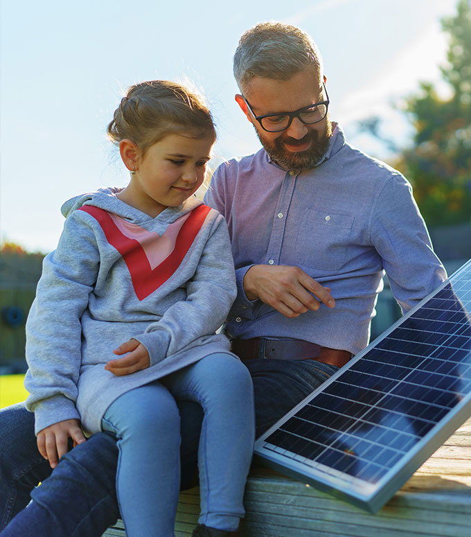 A dad is telling his little daughter about solar while holding a solar panel.